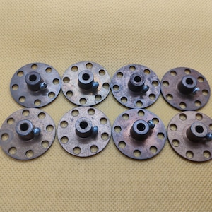 May include: Eight vintage metal circular components with a central hub and multiple surrounding holes. Each component has a small screw. The components are arranged on a yellow-tan surface.