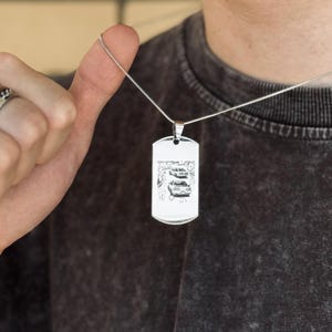 Op de afbeelding: Zilverkleurige hondenpenning hanger met een gedetailleerde zwarte afbeelding van twee auto's. De hanger hangt aan een dunne zilveren ketting. De tag is rechthoekig met afgeronde hoeken.