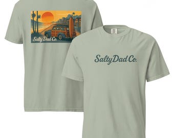 May include: Two light green t-shirts. One features a sunset scene with a wood-paneled car and surfboard, with "Salty Dad Co." below. The other shirt has "Salty Dad Co." in script across the chest.