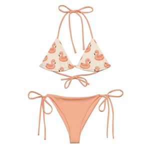 May include: A two-piece bikini set. The top is a halter style with a cream background and a pattern of pink flamingo floaties. The bottom is solid peach. Both pieces have tie closures.