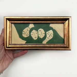 K&ouml;nnte beinhalten: Gerahmtes Gem&auml;lde mit einer Gruppe stilisierter Gesichter mit geschlossenen Augen. Das Kunstwerk ist haupts&auml;chlich gr&uuml;n und beige, mit einem goldfarbenen Rahmen. Das Gem&auml;lde zeigt eine Nahaufnahme der Gesichter, wobei Haare und Kleidung der Figuren verschmelzen.