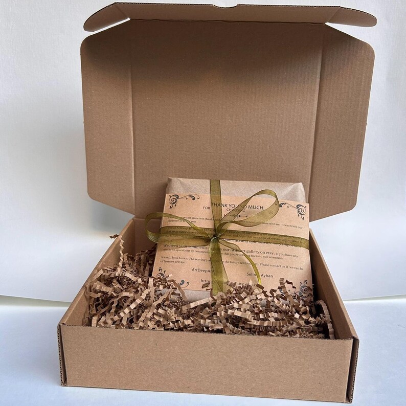 Pu&ograve; includere: Una scatola di cartone marrone aperta, che rivela un pacco avvolto e legato con un nastro verde. Il pacco &egrave; annidato in trucioli di carta marrone. Il pacco ha un'etichetta stampata che dice "THANK YOU SO MUCH".