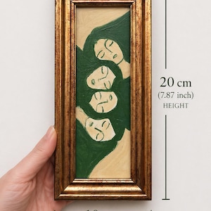 K&ouml;nnte beinhalten: Gerahmtes Gem&auml;lde mit vier stilisierten Gesichtern mit geschlossenen Augen, vor einem gr&uuml;nen und beigen Hintergrund. Der goldfarbene Rahmen ist 10 cm breit und 20 cm hoch. Das Kunstwerk hat eine Vintage-&Auml;sthetik.