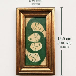 K&ouml;nnte beinhalten: Ein gerahmtes Kunstwerk mit einem Gem&auml;lde von vier stilisierten Gesichtern mit geschlossenen Augen. Das Gem&auml;lde verwendet Gr&uuml;n- und Cremet&ouml;ne und ist in einem goldfarbenen Rahmen eingefasst. Das Kunstwerk ist 10 cm breit und 15,5 cm hoch.