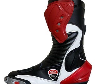 Könnte beinhalten: Motorradstiefel in Schwarz, Weiß und Rot mit dem Ducati Corse Logo. Der Stiefel hat einen roten Schienbeinschutz, weiße Akzente und eine verstärkte Zehenpartie. Entwickelt für das Motorradfahren, bietet er Schutz und Stil.