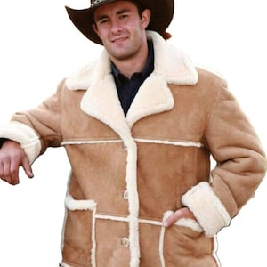 Puede incluir: Chaqueta de ante marrón claro con forro y ribete de borrego color crema. La chaqueta tiene cierre de botones, dos bolsillos delanteros y un cuello ancho. La persona de la imagen lleva un sombrero de vaquero marrón.