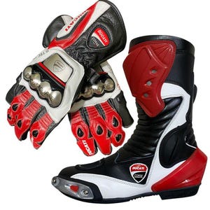 Puede incluir: Guantes y botas de moto negros, blancos y rojos. Los guantes tienen secciones rojas para los dedos y la palma, detalles blancos y protectores de nudillos plateados. La bota es negra con detalles blancos y rojos, con el logo "Ducati Corse".