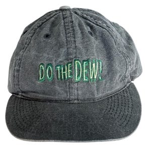 Puede incluir: Gorra de béisbol gris con visera curva. El texto "DO THE DEW!" está bordado en verde en la parte delantera. La gorra tiene un botón en la parte superior y un aspecto ligeramente descolorido.