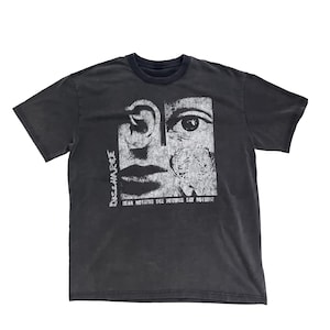 May include: Dark grey t-shirt with a distressed graphic. The graphic features a split face design with an ear, eye, and mouth, and the text "DISCHARGE" and "HEAR NOTHING SEE NOTHING SAY NOTHING" in white.