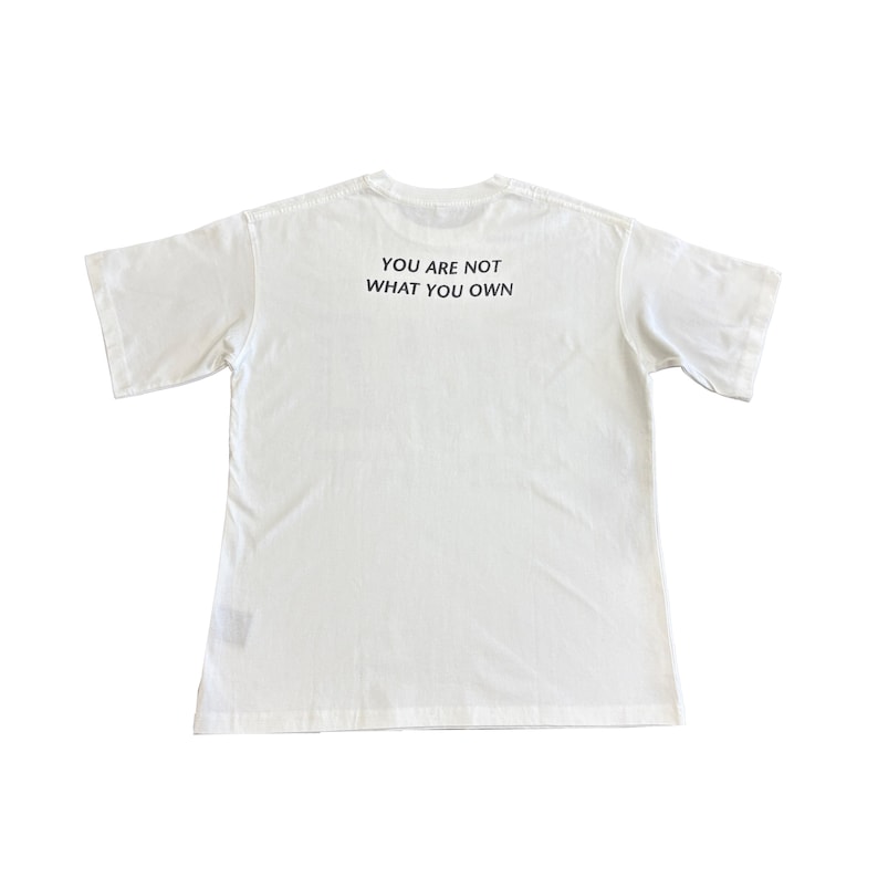May include: A white t-shirt with short sleeves. The text "YOU ARE NOT WHAT YOU OWN" is printed in black on the back of the shirt. The shirt is made of a soft, comfortable material.