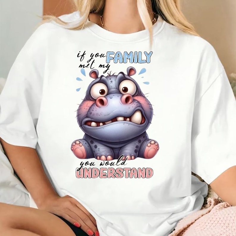 May include: White t-shirt featuring a cartoon hippo with a worried expression. The hippo is blue and pink, with the text "if you met my FAMILY you would UNDERSTAND" in blue and pink lettering.
