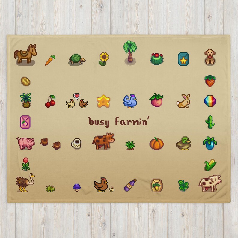 Op de afbeelding: Een beige deken met pixelafbeeldingen van boerderijdieren, gewassen en andere boerderijgerelateerde items. De deken heeft de tekst "busy farmin'" in het midden. De deken is gemaakt van een zacht materiaal.