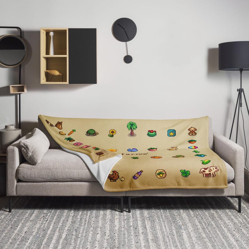 Op de afbeelding: Een beige sprei met pixelafbeeldingen met boerderijthema's, waaronder een paard, wortel, schildpad, zonnebloem en diverse voedingsmiddelen. Het woord "Farming" wordt ook weergegeven. De sprei ligt over een grijze bank.