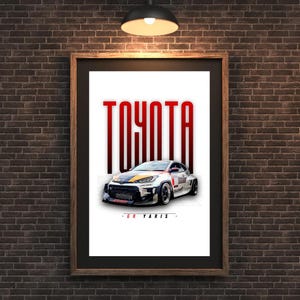 May include: Framed print featuring a Toyota GR Yaris race car. The word "TOYOTA" is in large red letters above the car. The car is white with black, yellow, and blue accents. The text "- GR YARIS -" is below the car.