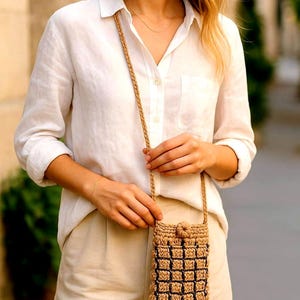 Può includere: Piccola borsa a tracolla intrecciata per telefono, di colore beige naturale con un motivo a griglia nero. La borsa ha una lunga tracolla intrecciata e una chiusura con bottone. Realizzata in materiale strutturato.