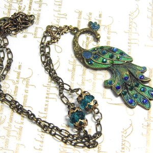 May include: A bronze peacock pendant necklace with green and blue enamel and crystal accents. The necklace features a double chain with two green crystal beads.
