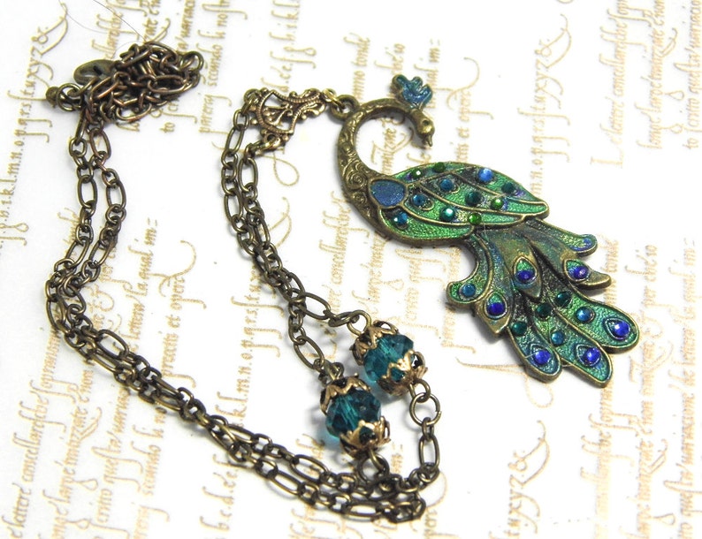 May include: A bronze peacock pendant necklace with green and blue enamel and crystal accents. The necklace features a double chain with two green crystal beads.