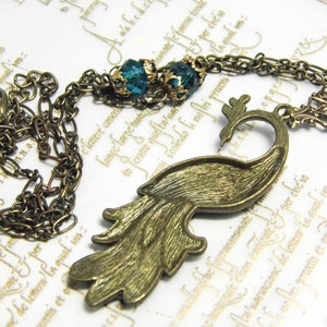 May include: A bronze peacock necklace with a chain and two teal blue gemstone accents.