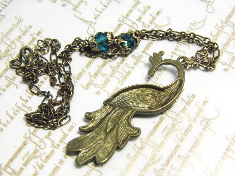 May include: A bronze peacock necklace with a chain and two teal blue gemstone accents.