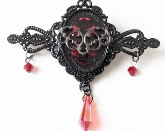 May include: Black metal brooch with a red glass center and dangling red crystals.