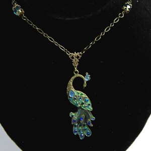 May include: A gold chain necklace with a peacock pendant. The peacock is made of metal and has blue and green enamel with rhinestones. The chain has two blue rhinestone accents.