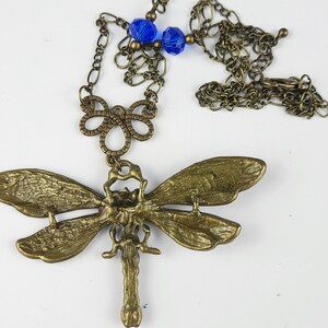 May include: A gold-toned dragonfly pendant necklace with blue glass beads. The dragonfly has intricate details and is attached to a delicate chain.