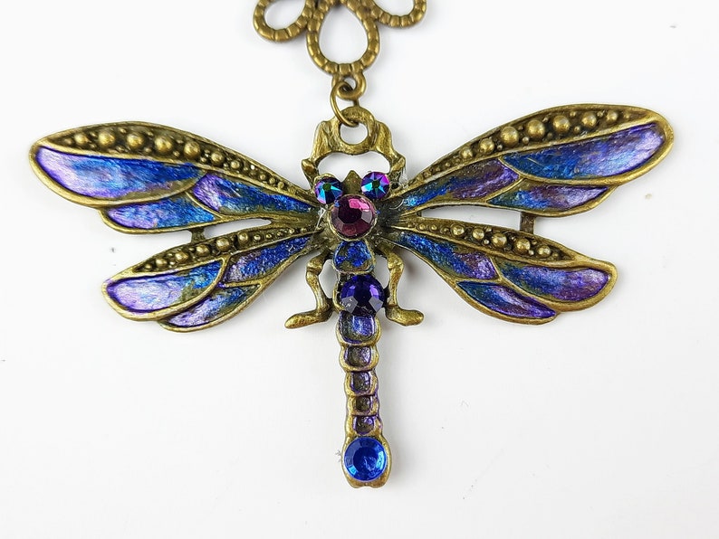 May include: A blue and purple dragonfly pendant with jeweled accents. The dragonfly is made of metal and has a detailed design.