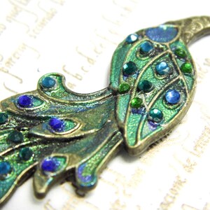 May include: A peacock-shaped metal charm with green and blue enamel and rhinestones. The charm is in a vintage style and has a detailed design.