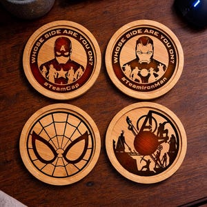 Könnte beinhalten: Vier runde Untersetzer aus Holz mit Superhelden-Motiven. Zwei Untersetzer zeigen Captain America und Iron Man mit dem Text "Whose side are you on?" und Team-Hashtags. Ein Untersetzer zeigt eine Spinnennetz-Maske und einer zeigt Silhouetten.