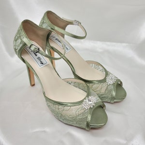 A pair of sage green high heeled platform lace shoes with an ankle strap and a crystal design on the front of the peep toe shoe