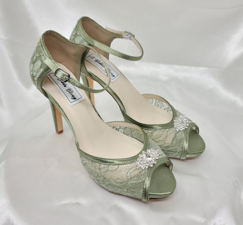 A pair of sage green high heeled platform lace shoes with an ankle strap and a crystal design on the front of the peep toe shoe