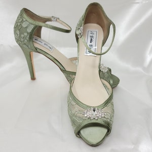 A pair of sage green high heeled platform lace shoes with an ankle strap and a crystal design on the front of the peep toe shoe