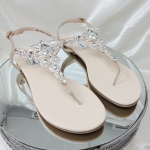 a pair of flat heel ivory sandals with crystals on the straps of the sandals