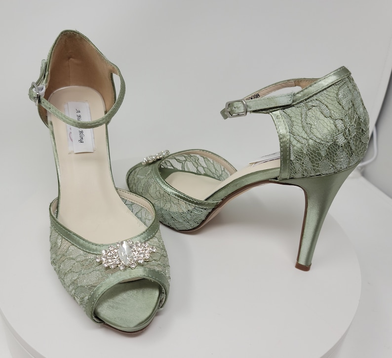 A pair of sage green high heeled platform lace shoes with an ankle strap and a crystal design on the front of the peep toe shoe