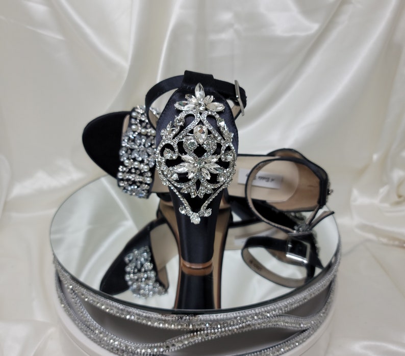 A pair of high black block heel shoes with an ankle strap and a crystal and pearl design on the front toe strap of the shoes and a large crystal design on the back heel of the shoes