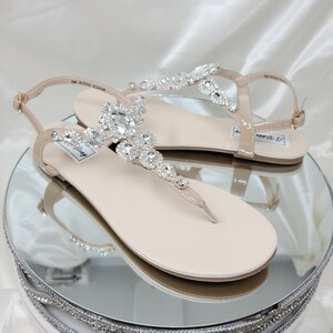 a pair of flat heel ivory sandals with crystals on the straps of the sandals