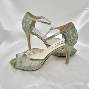 A pair of sage green high heeled platform lace shoes with an ankle strap and a crystal design on the front of the peep toe shoe