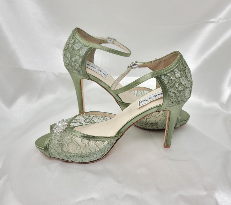 A pair of sage green high heeled platform lace shoes with an ankle strap and a crystal design on the front of the peep toe shoe