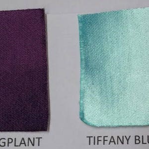 Op de afbeelding: Twee stoffen stalen, &eacute;&eacute;n aubergine en de andere Tiffany blauw, worden getoond tegen een witte achtergrond. De woorden "EGGPLANT" en "TIFFANY BLUE" staan eronder gedrukt. De stoffen hebben een lichte glans.