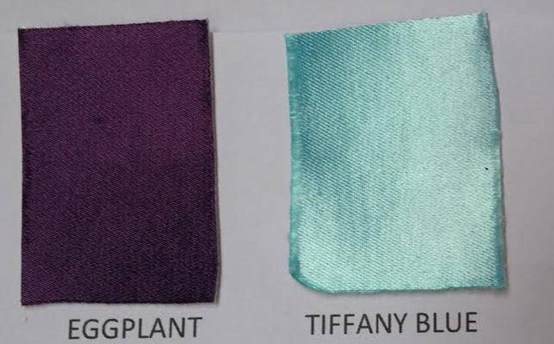 Op de afbeelding: Twee stoffen stalen, &eacute;&eacute;n aubergine en de andere Tiffany blauw, worden getoond tegen een witte achtergrond. De woorden "EGGPLANT" en "TIFFANY BLUE" staan eronder gedrukt. De stoffen hebben een lichte glans.