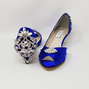 A pair of royal blue satin kitten heel shoes with a peep toe and a pearl and crystal design on the front of the shoes and a large crystal design on the back heel of the shoes