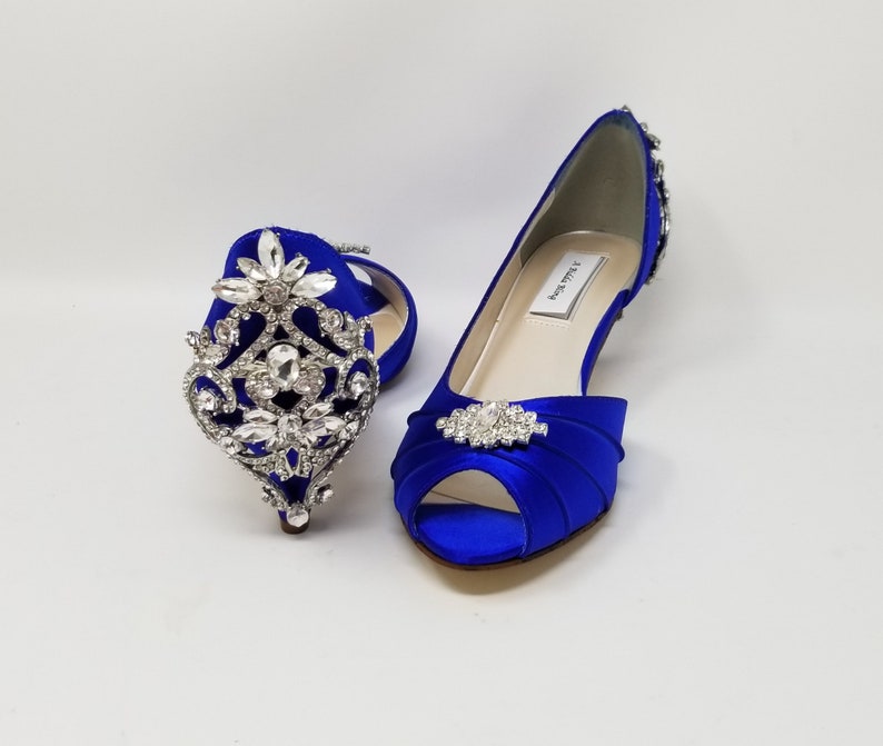 A pair of royal blue satin kitten heel shoes with a peep toe and a pearl and crystal design on the front of the shoes and a large crystal design on the back heel of the shoes