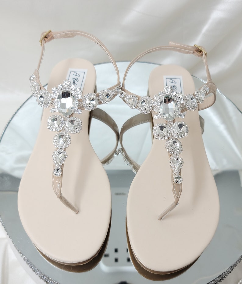 a pair of flat heel ivory sandals with crystals on the straps of the sandals