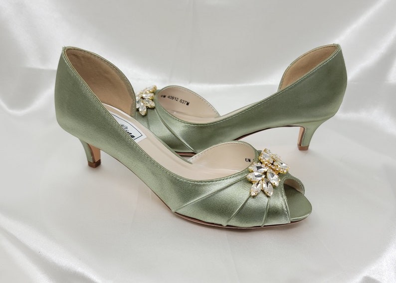 a pair of sage green satin kitten heel shoes with a peep toe and a gold and crystal design on the front of the shoes