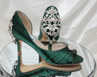 May include: A pair of emerald green satin high heel shoes with a peep toe and a jeweled embellishment on the top of the shoe.