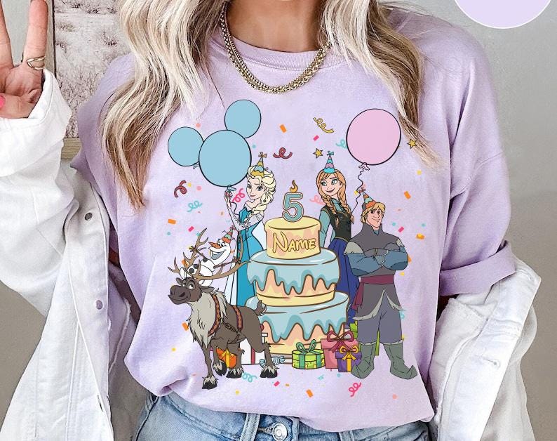 Puede incluir: Una sudadera lila con un gr&aacute;fico colorido de personajes de la pel&iacute;cula Frozen. El dise&ntilde;o incluye a Elsa, Anna, Kristoff, Olaf y Sven, junto con una tarta de cumplea&ntilde;os, globos y confeti. El n&uacute;mero 5 y la palabra "Name" tambi&eacute;n son visibles.