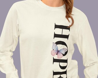 Könnte beinhalten: Cremefarbenes Langarmshirt mit dem Wort "HOPE" vertikal in Schwarz gedruckt. Ein Aquarell-Schmetterling in Rosa und Blau befindet sich neben dem Buchstaben "O". Das Shirt hat einen Rundhalsausschnitt und eine lockere Passform.
