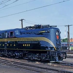 May include: A vintage black and gold Pennsylvania Railroad electric locomotive, number 4935, on tracks. The locomotive has a streamlined design with yellow stripes and the words "PENNSYLVANIA" and the number "4935" in gold lettering.