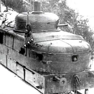 May include: A vintage armored train, captured in a black and white photograph. The train features a rounded turret, gun ports, and a boxy body. It is set against a snowy backdrop, suggesting a winter environment. The train's design indicates a historical military application.