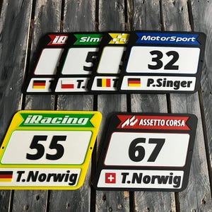 May include: A collection of racing-themed plaques with black borders. Each plaque features a number, driver's name, and a flag. The plaques are labeled with "iRacing", "Sim", "Motorsport", and "Assetto Corsa".